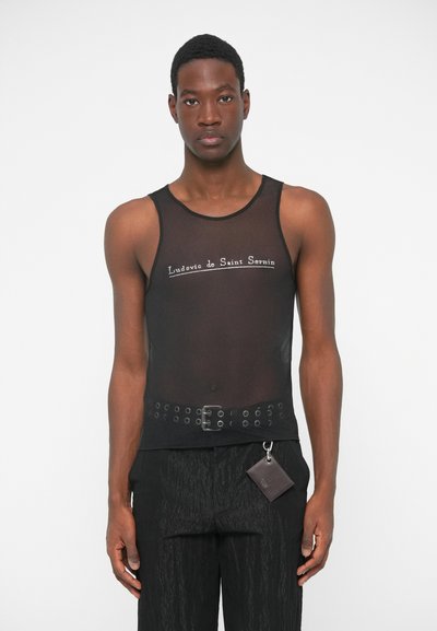 Μαύρο διχτυωτό τοπ με κεντημένο το όνομα της μάρκας. Συνδυασμένο με μαύρα παντελόνια με υφή, ζώνη με τρουκς και μίνι πορτοφόλι.