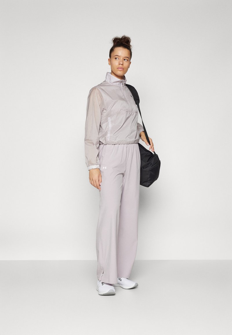 Leichte, pastellgraue Jacke mit elastischem Bund und Bündchen, kombiniert mit passenden grauen Hosen und weißen Sneakers. Schwarze Umhängetasche.