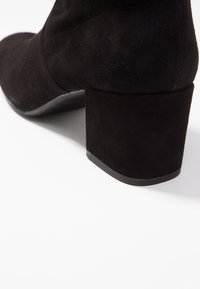 Bottine en daim noir avec un talon carré, texture lisse et détails de couture subtils sur le dessus.