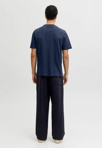 Camiseta de algodón azul marino con mangas cortas y cuello redondo, combinada con pantalones oscuros de corte holgado con bolsillos laterales.