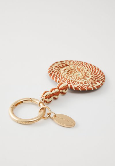 Gewebter Schlüsselanhänger in Orange und Creme mit einem kreisförmigen geflochtenen Design, ausgestattet mit einem goldfarbenen Metallring und einem Anhänger, der mit "VANESSA BRUNO" graviert ist.