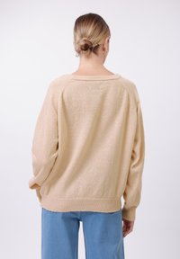 Beige oversized genser med ribbestrikket kant og mansjetter; myk tekstur; rund hals; bakside vist, kombinert med lyseblå vide jeans.