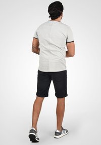 T-shirt gris à manches courtes avec des accents noirs, associé à un short en denim noir retroussé et des chaussures grises avec une semelle blanche et des rayures.