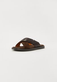 Brune sandaler med glatte og suedelignende krydsede remme, orange indvendig foring og en flad sort sål.