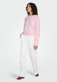 Light pink sweater with a relaxed fit, long sleeves, and ribbed cuffs, paired with white straight-leg pants and burgundy slip-on shoes.