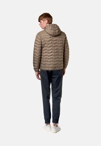 Giacca imbottita con cappuccio di colore marrone chiaro, con un design a trapunta ondulata, abbinata a pantaloni scuri e sneakers bianche, vista da dietro.