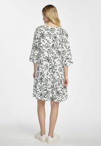 Biała sukienka z czarnym kwiatowym wzorem, rękawami 3/4, warstwowym fasonem i okrągłym dekoltem. Połączona z białymi trampkami.