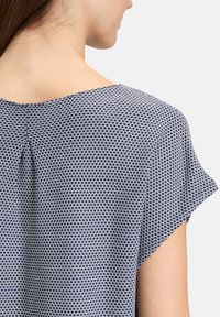 Top a maniche corte con un motivo geometrico blu navy e bianco, caratterizzato da una piega sul retro, con una vestibilità comoda e una texture di tessuto morbido.