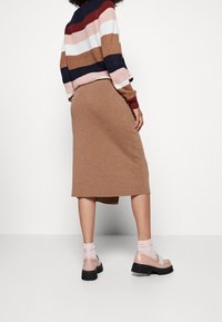 Stickad randig tröja i blått, rosa, rött och brunt; brunt knälångt kjol; rosa ankelsockor; kraftiga svarta skor med en beige ovandel.