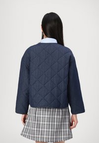 Donkerblauwe gewatteerde jas met een ronde hals en brede mouwen, gecombineerd met een geruite rok. Geweven stof in een klassiek patroon.
