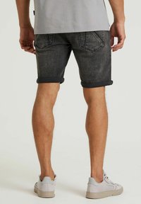 Shorts in denim grigio scuro con orli arrotolati, dotati di tasche posteriori e una finitura leggermente testurizzata. Visibili un paio di sneakers grigio chiaro.