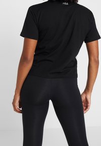 Černé bavlněné tričko s krátkým rukávem a kulatým výstřihem, na zadní straně se nachází malé logo "Fila". Spárováno s černými legínami.