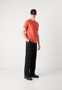 Tricou scurt cu mânecă portocalie și guler rotund, pantaloni negri largi, pantofi chunky negri și o șapcă neagră cu logo alb.
