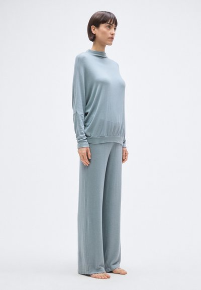 Világoskék, egymással harmonizáló otthoni ruházati szett, amely laza felsőből áll magas nyakkivágással és széles szárú nadrágból, puha, sima anyagból készült.