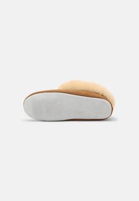 Pantoufle tan avec un dessus en fourrure beige épaisse et duveteuse, extérieur en daim et semelle en caoutchouc grise. Forme moulée pour le confort et le soutien.