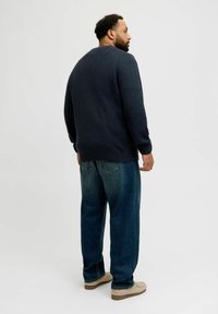 Navy knitted sweater with a textured design, paired with loose-fit blue denim jeans. The model is wearing light-brown shoes.