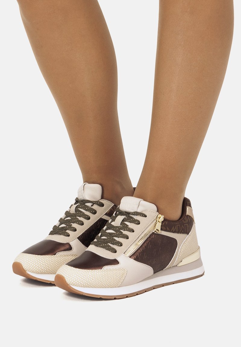 Zapatillas con una parte superior de malla beige, acentos de cuero marrón, cordones verdes y un zipper en el costado. Suela de goma con un acabado texturizado.