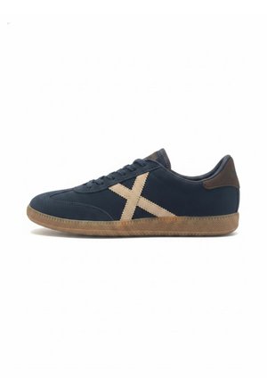 Granatowy niski sneaker z beżowym krzyżowym detalem po boku, brązową łatką na pięcie i jasnobrązową teksturowaną podeszwą.