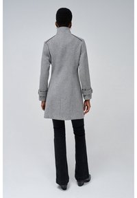 Cappotto grigio a spina di pesce con colletto alto, vestibilità sagomata e maniche a polsino. Abbinato a pantaloni neri svasati e stivali neri chunky.