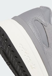 Gray sneaker featuring a combination of leather and textile materials. White midsole and black rubber outsole with textured detailing.
