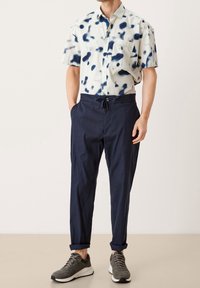 Kortärmad skjorta i lätt tyg med blå sprutmönster, kombinerad med marinblå byxor med dragsko. Bärs med grå sportskor.