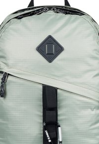 Grøn stofrygsæk med en tekstureret overflade, diamantlogo-patch, en lynlåslomme, og en sort webbingrem med en karabinhage.