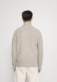 Pull en tricot gris clair avec col montant, tissu texturé et poignets et ourlet côtelés. Offre une coupe décontractée et un design simple.