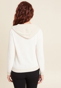 Pull en tricot crème clair avec une capuche beige contrastante, des poignets et un ourlet côtelés ; texture douce visible sur le tissu.
