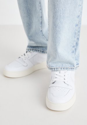 Valged nahast madala profiiliga spordijalatsid, millel on perforatsiooniga varvas, lame paelad ja minimalistlik disain. Koos helesiniste teksadega.