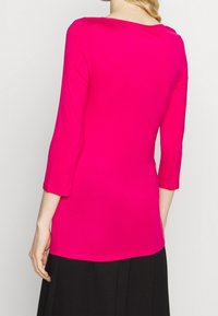 Fuchsia langærmet bluse lavet af glat, strækbart stof. Har bådudskæring og tapered ærmer, der går ned til hoften.