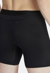 Svarta bomullsboxershorts med en slät textur, figurnära design och en mjuk elastisk midja. Synliga sömmar längs kanterna.