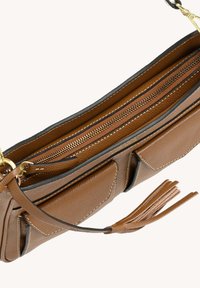 Sac à main en cuir marron avec deux poches avant, fermeture à glissière dorée et gland en cuir sur la sangle, sur fond blanc.