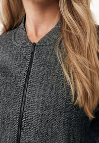 Veste à motif chevron noir et blanc avec un col arrondi et une fermeture éclair complète. Présente un tissu texturé et une coupe ajustée.