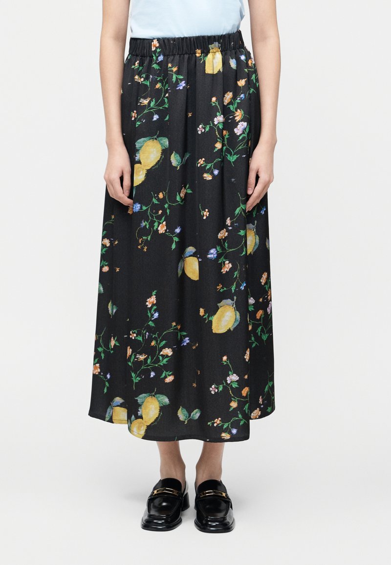 Μαύρη maxi φούστα με κίτρινα λεμόνια και μικρά λουλουδένια σχέδια, ελαστική μέση, φορεμένη με μαύρα μοκασίνια και ανοιχτό μπλε τοπ.