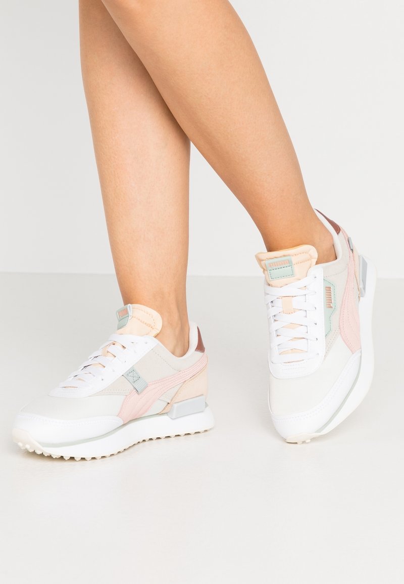 Baskets blanches avec des touches pastel de rose, bleu et pêche, présentant une surface texturée et une semelle rembourrée pour le confort. Design lacé.