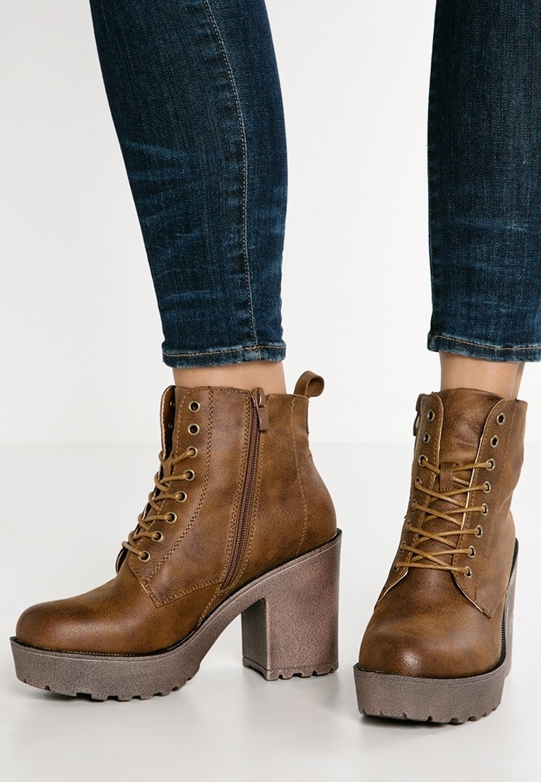 Brązowe skórzane botki za kostkę z teksturowanym wykończeniem, sznurówką z przodu, zapięciem na zamek oraz masywnym obcasem z kontrastującą podeszwą.