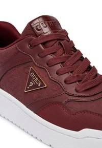 Sneaker in cuoio bordeaux con un motivo testurizzato, logo triangolare dorato e suola bianca, dotato di lacci coordinati e collo imbottito.