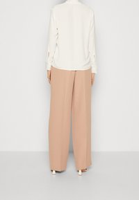 Krémová blůza s dlouhými rukávy a výřezy na zápěstí, doplněná béžovými širokými kalhotami s vysokým pasem a bílými blokovými podpatky.