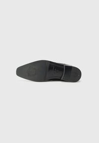 Suela de zapato de cuero negro con textura suave, punta redondeada y logo embosado. Presenta una curva sutil y un diseño de tacón pequeño.