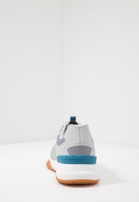 Grijze sportieve schoen met een bovenwerk van mesh, blauwe accenten, een rubberen zool en een trekband, met gestructureerde patronen op het materiaal.