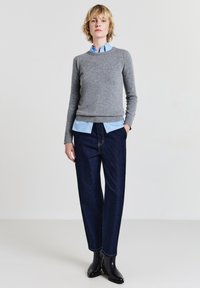 Pull en maille gris porté sur une chemise col en bleu clair, assorti à un jean droit bleu foncé et des bottines noires, design minimaliste.