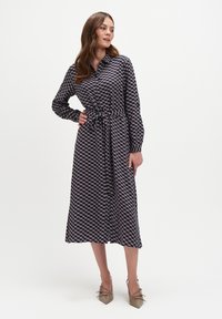 Sukienka w morskim wzorze z długimi rękawami, zapięciem na guziki z przodu, z paskiem w talii i długości do połowy łydki, zestawiona z beżowymi szpilkami w szpic.