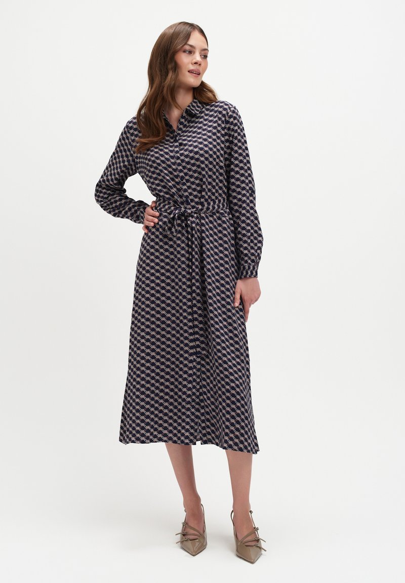 Sukienka w morskim wzorze z długimi rękawami, zapięciem na guziki z przodu, z paskiem w talii i długości do połowy łydki, zestawiona z beżowymi szpilkami w szpic.