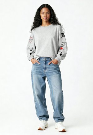 Grijze sweatshirt met lange mouwen featuring verschillende graphics, gecombineerd met losse lichtblauwe jeans en witte sneakers.