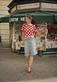 Rdeča majica s kratkimi rokavi s cvetličnim vzorcem, v kombinaciji s svetlim denim krilom in rdečimi čevlji. Dodatki vključujejo pas in nogavice z vzorcem.