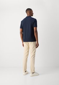Marineblå polo med korte ærmer, parret med lyse beige bukser. Outfittet har en afslappet pasform og enkel design, suppleret med hvide sneakers.