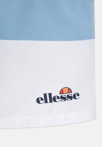Modré a biele športové kraťasy s hladkou textúrou; obsahujú logo na spodnej časti. Dizajn zahŕňa farebné blokovanie.