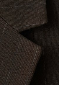 Gros plan d'un tissu de costume marron foncé avec de fines rayures claires subtiles et des revers qui se superposent.