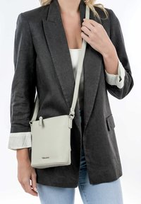 Borsa a tracolla in pelle grigia chiara con superficie texturizzata, forma rettangolare, tracolla regolabile e dettagli in metallo argentato.