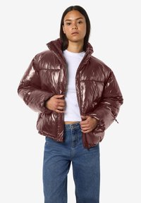 Blizgi bordo spalvos pūsta striukė su aukštu apykakliu, kvadratine forma ir elastinėmis rankogaliais. Dėvima ant balto marškinėlių ir derinama su mėlynais džinsais.